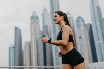 Sport and lifestyle concept. Young fitness woman doing running outdoors on skyscrapers background