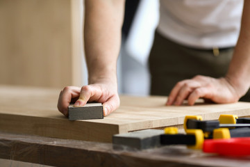 Carpenter man grinds wooden sheet in workshop