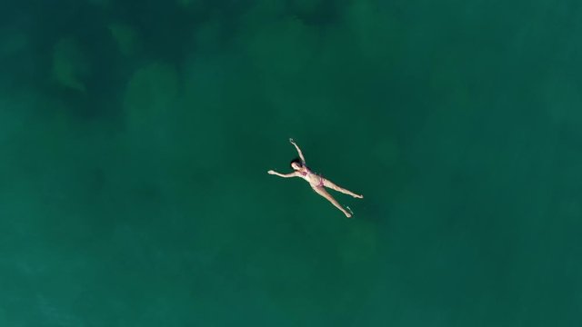 Relaxed woman lie on sea water with arms and hands stretched out, camera fly up, nobody around. Warm and calm waters of Aegean Sea, female swimmer take rest