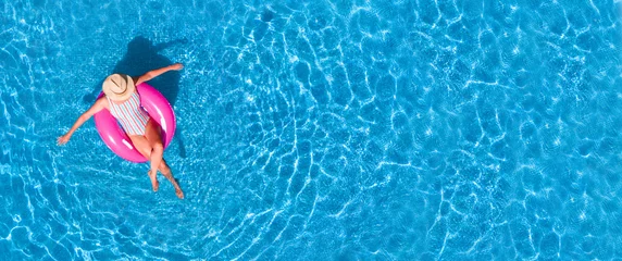 Zenith-Luftaufnahme eines Swimmingpools im Sommer. Junges Mädchen in einem Badeanzug und einem Hut, der mit rosa Donut schwimmt. © Lia Aramburu