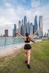 Fototapeta na wymiar Rear view of young fitness woman with raised hands look at skyscrapers. Sport success concept.