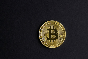 Front side of a physical gold Bitcoin on black background with copy space