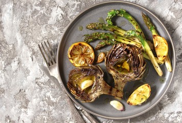 artichoke and asparagus grill. Tasty vegetables are first cooked for a couple, then fried on a grill, poured with olive oil and spices. spring vegetables. background concrete. top view.  copy space. 