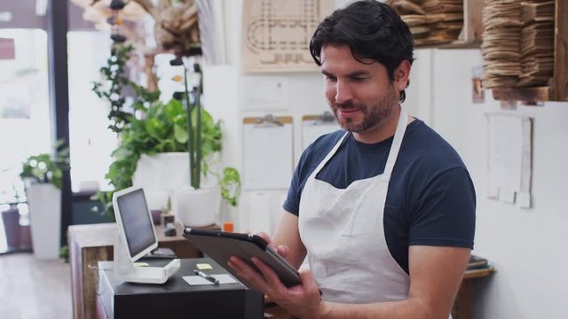 Portrait of male owner of florists shop working on digital tablet behind sales desk - shot in slow motion