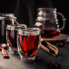 Cup of freshly brewed black tea, dark moody, tea ceremony. Hot water is poured from the kettle into a flass cup on wooden tray, black concrete background.