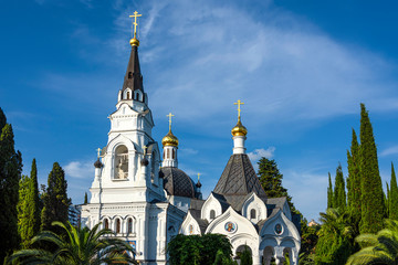Fototapeta na wymiar Russia, Black Sea, Sochi: Famous Cathedral of St. Michael the Archangel in the city center of the Russian town with golden cross, green garden, white facade, blue sky - travel history