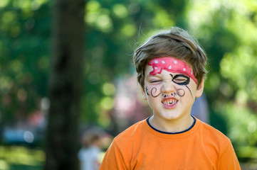 Child making funny faces. Kid with a pirate painting on his face.