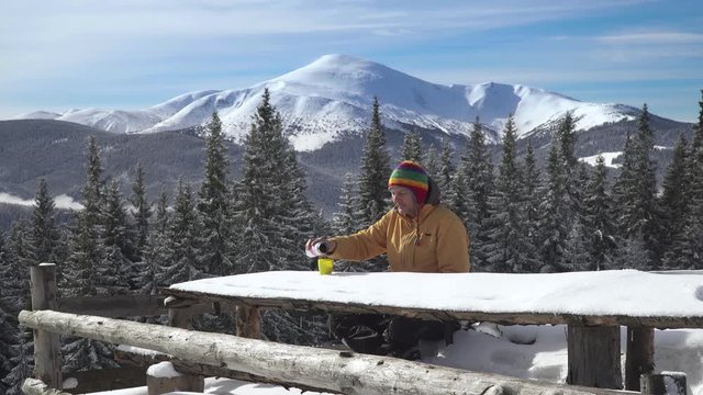 A man sits and drinks tea against the backdrop of the winter landscape. The concept of travel and active lifestyle. Carpathian mountain range. 4K