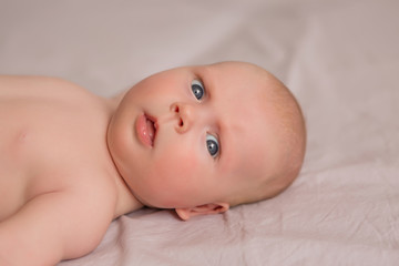 Happy 3 months old baby smiling, lying on white bed