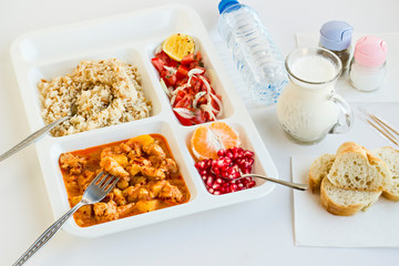 Traditional Turkish Meal with chicken potato,rice,tomato salad and fruits in the white portion food tray.Table d'hote-known TABLDOT in TR-Designed on the white surface.