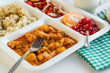 Traditional Turkish Meal with chicken potato,rice,tomato salad and fruits in the white portion food tray.Table d'hote-known TABLDOT in TR-Designed on the white surface.