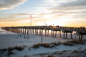 sunset at panama city beach pier with sun going down behind pier and beautiful clouds and sky and ocean