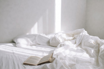 In the bright bedroom, an open old book is lying on the bed. Against the background of the sun's rays
