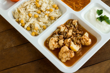 White food tray (table d'hote) with traditional Turkish meals and a bottle of water on wooden table, top view
