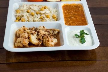 White food tray (table d'hote) with traditional Turkish meals and a bottle of water on wooden table, top view