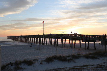 Obraz premium sunset at panama city beach pier with sun going down behind pier and beautiful clouds and sky and ocean