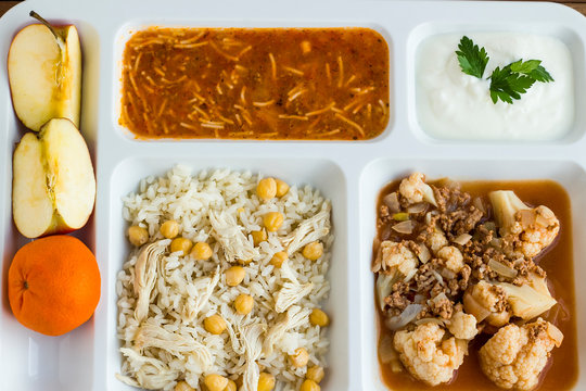 Traditional Turkish rice made with chickpeas and chicken, Turkish vermicelli soup and cooked cauliflower with tomato paste and mince, in white lunch tray (table d'hote) with fruits and yogurt