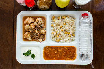White food tray (table d'hote) with traditional Turkish meals and a bottle of water on wooden table, top view