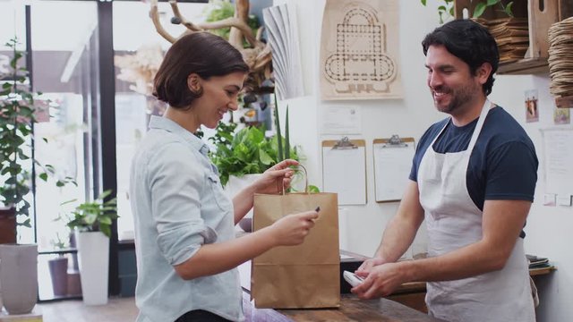 Woman in florists shop making contactless payment at sales desk - shot in slow motion