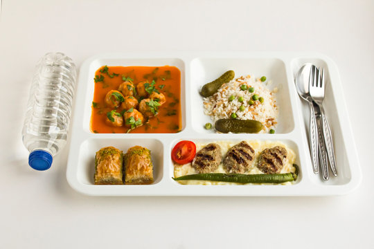 Traditional Turkish meals,meatballs soup,rice,mashed potatoes,grilled meatball and two slices of baklava in  food tray with water.Table d'hote (known Tabldot in Turkey) on white surface.