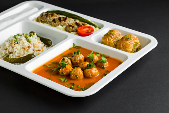 Traditional Turkish meals,meatballs soup,rice,mashed potatoes,grilled meatball and two slices of baklava in  food tray.Table d'hote (known Tabldot in Turkey) on white surface.