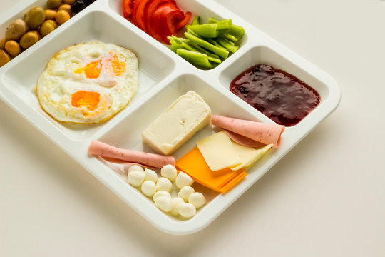 Traditional Turkish breakfast with cheese, salami, pepper, jam, egg, tomato and olives in a plastic white food tray (table d'hote) on white 