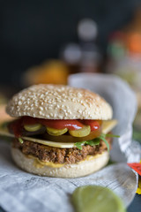 Closeup view of a quorn burger on a wooden table. Some of ketchup, mustard, vegan cheese and some lettuce accompany the meatless meat.