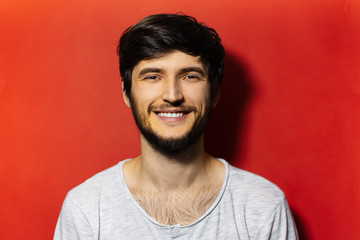 Fototapeta premium Portrait of young smiling guy dressed in white shirt, isolated on background of red color.
