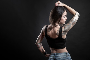 Fototapeta na wymiar Bella Mora tatuata mora indossa una canotta nera e posa in uno studio isolata su sfondo nero