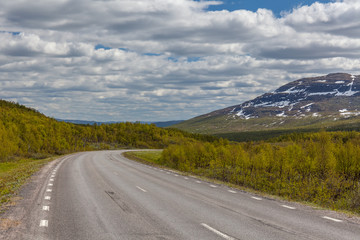 straight and lonely road between swedish mountains under cloudy sky, selective focus, Swedish mountains border with norway. snow peaks