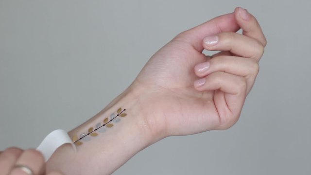 hand of a young woman wih gold floral leaves temporary tattoo on her wrist