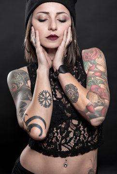 Donna tatuata mora con capelli a cashetto indossa una canotta nera , isolata su sfondo nero