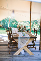 Wedding or dinner reception table, decorated in rustic style, outdoors in stylish tent. Reception on open air, rustic wedding