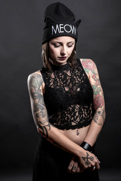Ragazza  tatuata con cuffietta indossa una canotta nera ,e posa con aria seria  isolata su sfondo nero