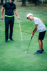 Fototapeta premium Golf Putting Training. Golf Instructor with Young Boy Practicing on the Putting Green