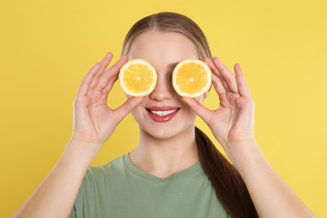 Young woman with cut lemon on yellow background. Vitamin rich food