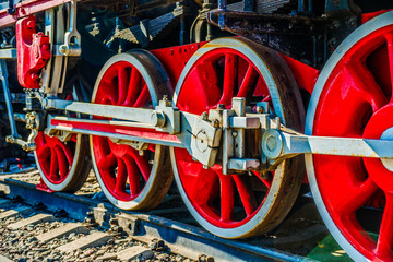 Red driving wheels of a vintage steam engine locomotive. Driving rods, drives, cranks and other parts. The history of railway transport.