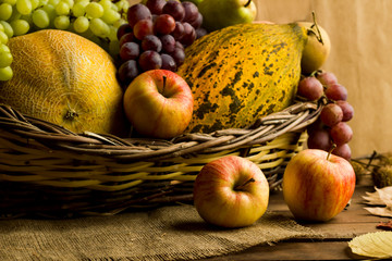 Fresh,ripe melons, grapes, and apples in a wicker basket on wooden table.Conceptual image of harvest season or Thanksgiving.