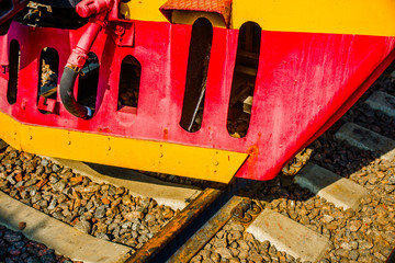 Cowcatcher of a vintage diesel engine locomotive painted red and yellow. Rusty rails. The history of railway transport.