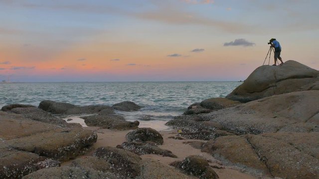 Photographer finds the location for taking nature landscape photo on the beach rock with evening colorful sky 