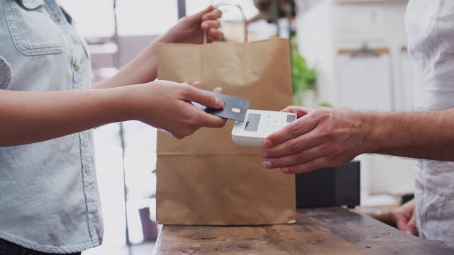 Close up of woman in store making contactless payment at sales desk holding card to reader - shot in slow motion