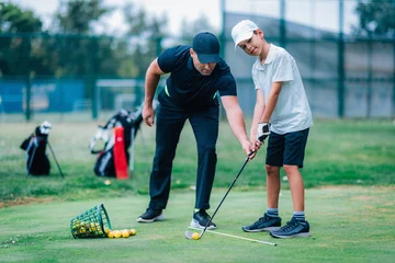 Poster Personal golf lesson. Golf instructor with young boy on a golf driving range. © Microgen