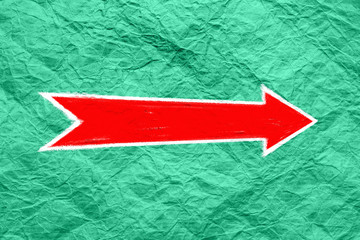Arrow on a green textured surface. Red arrow pointer is drawn on green crumpled paper. Direction indicator. Signs and pointers.