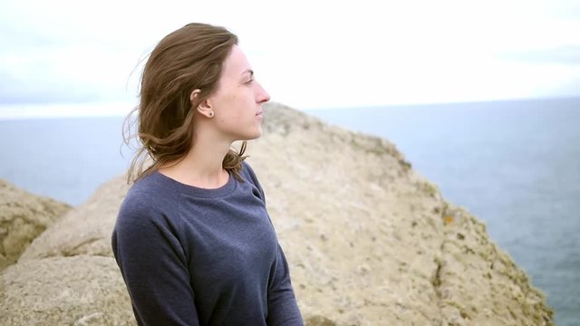 A young woman sits on the edge of a mountain cliff and looks at the ocean, sea. Travel, tourism