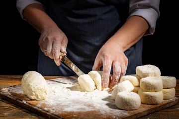 Female hands knead the dough on a wooden antique table on a dark background, close-up, shallow depth of field, beautiful directional lighting. Concept of home baking and comfort.