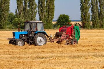 Fototapeta na wymiar tractor makes big straw roll on yellow field at summer day