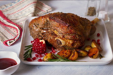 Leg of lamb served with potatoes, pomegranate seeds and rosemary on white plate, horizontal image