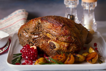 Leg of lamb served with potatoes, pomegranate seeds and rosemary on white plate, horizontal image
