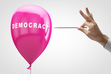 Concept: Threat of Democracy. Inflatable pink balloon and a needle in hand.