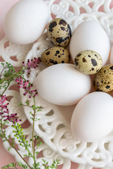 Mix of quail eggs and hen eggs on white vintage plate